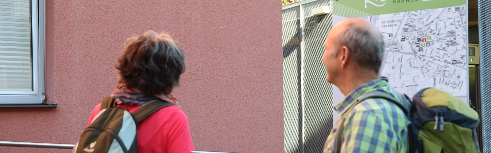Zwei Personen schauen das Schild des Zähringer Wanderwegs am Rathaus an