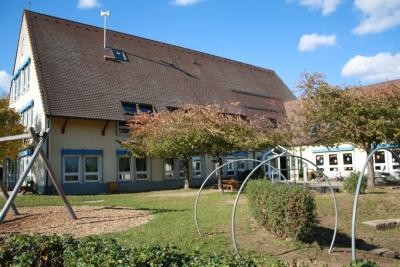 Eine große Gruppe von Kindern mit Erziehern. Die Kinder sitzen am Boden und auf Stühlen. Auf einem bunten Banner steht - Herzlich Willkommen - Bienvenue!
