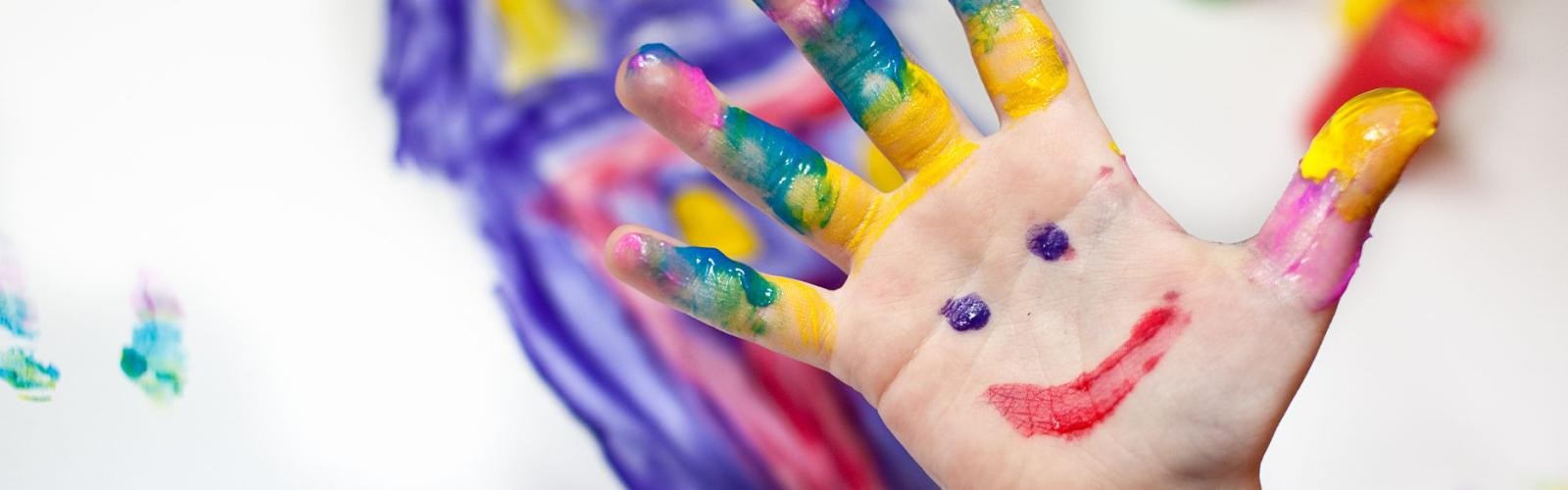 Eine mit Fingerfarben bemalte Kinderhand als Gesicht.