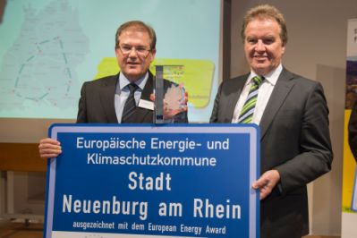 Links Bürgermeister Schuster, rechts Herr Schoofs, halten in den Händen die eea Auszeichnung
